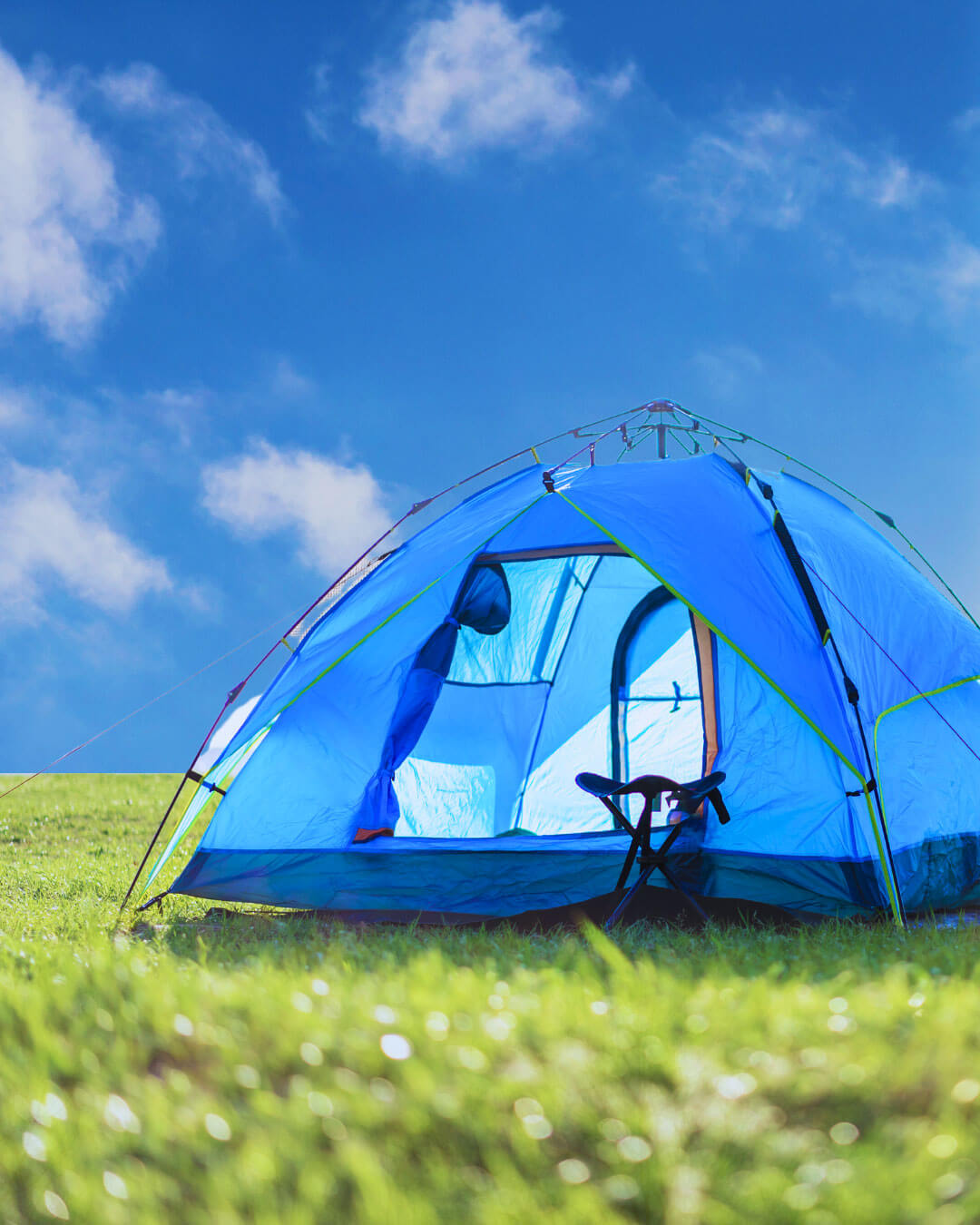 small blue tent on green grass with blue sky